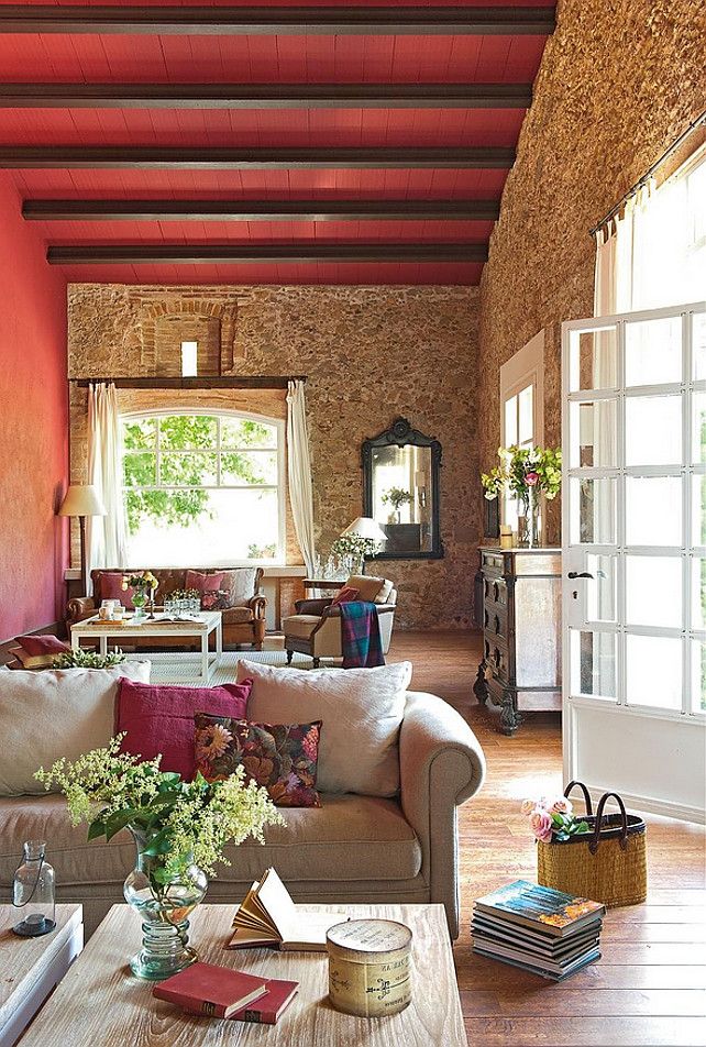 A Provence living room with stone walls, bright red touches, vintage furniture and large windows
