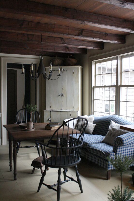 a rustic living room with wooden beams on the ceiling, a wooden dining set, cozy farmhouse furniture