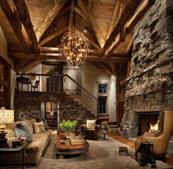 a rustic cabin living room with a fireplace clad with stone, a stone staircase and a large orb chandelier of wood