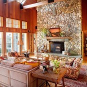 a stone fireplace, wooden walls, bright furniture and potted greenery and much natural light