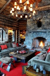 a bright cabin living room with wooden walls and a stone hearth, a reclaimed wooden table and a chandelier