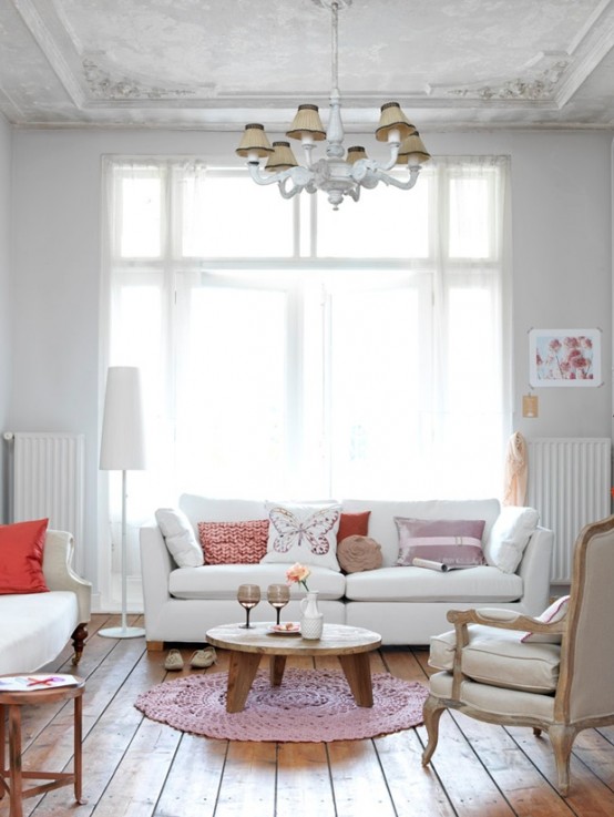 a delicate living room in neutrals, with vintage touches - white seating furniture, pink and coral pillows and a chic vintage chandelier