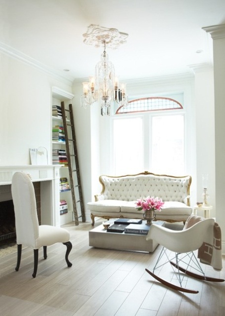 A chic and feminine living room done in neutrals, with refined furniture, built in shelves, a chic chandelier, a low coffee table and a fireplace