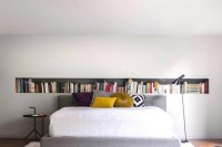 a contemporary bedroom with a long niche shelf, a bed with bold pillows, a black side table and black chair