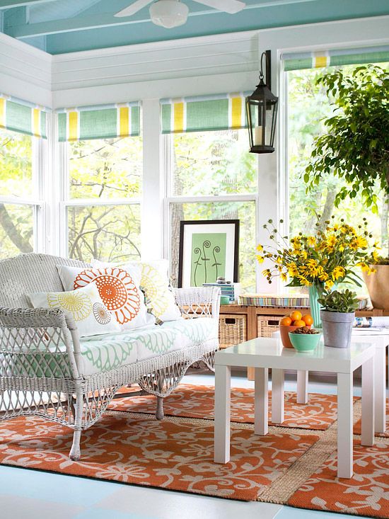 a colorful Scandinavian sunroom with a blue ceiling, white furniture, colorful textiles and potted greenery and blooms
