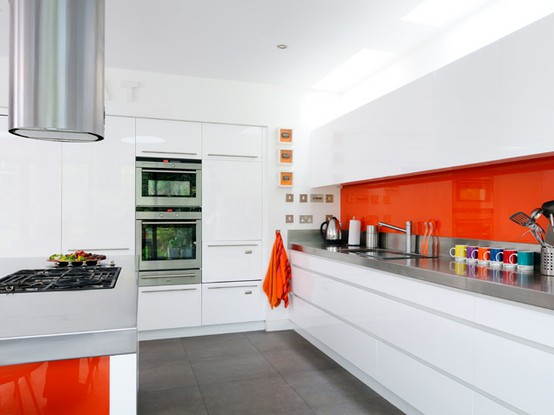 An all white minimalist kitchen with bold orange touches   a backsplash and sides for a cheerful and fun look