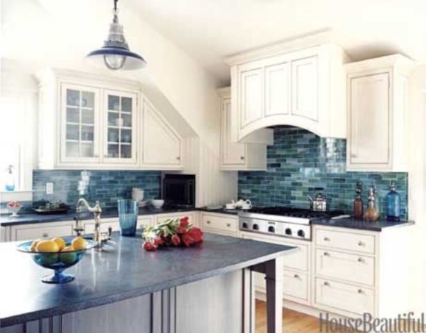 An ocean inspired kitchen with neutral shaker style cabinets, a gorgeous blue tile backsplash, a blue pendant lamp and a midnight blue kitchen island