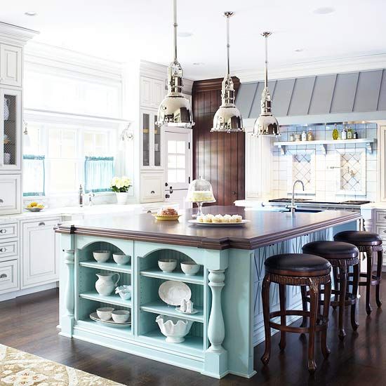 A catchy ocean inspired kitchen with white and grey shaker cabinets, ocean blue tiles over the cooker, a metal hood, a turquoise kitchen island and dark stained stools