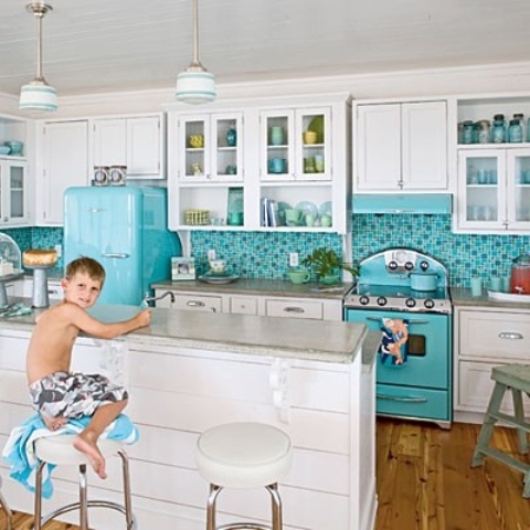 a colorful beach kitchen with white shaker cabinets, a bold turquoise tile backsplash and a matching cooker, a matching fridge and a large kitchen island