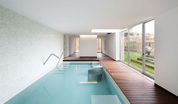 A minimalist pavilion with a large pool, a dark stained deck, lights and a glazed wall to enjoy the views of the garden