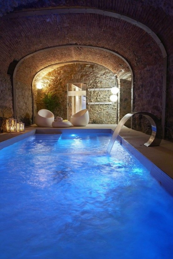 a home spa with an arched ceiling, a large blue pool with a faucet, some ultra-modern white furniture