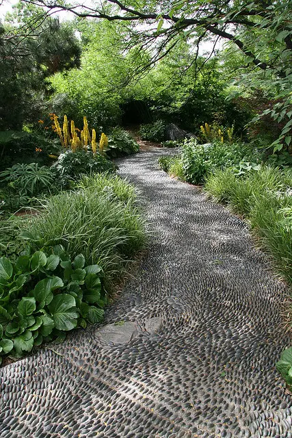 a simple black pebble garden pathway is a practical idea that highlights the greenery that lines it up