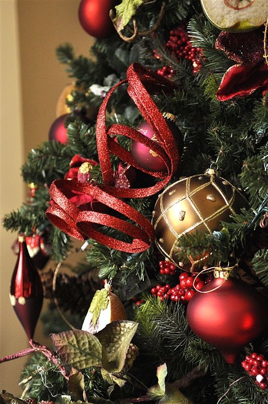 a Christmas tree decorated with red and gold ornaments, berries, foliage, glitter ribbons