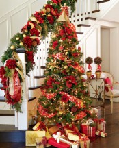 traditional gold and red Christmas decor – a Christmas tree with such decor and lights and railing decorated with evergreens, gold and red plus pinecones
