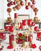red and gold glitter Christmas decor with ornaments hanging over the table, red glasss and gold candles and much more for the holidays