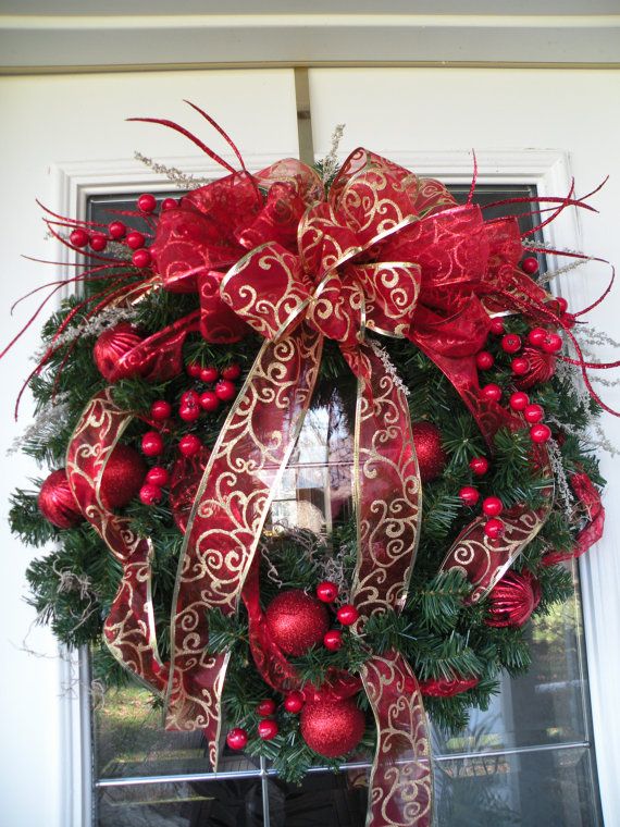 An evergreen wreath with red ornaments of various sizes and red and red and gold ribbons and bows