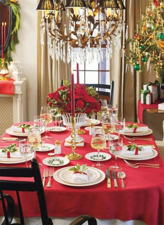 a chic Christmas tablescape with a red tablecloth, white porcelain, a lush red floral centerpiece and red candles, gold touches