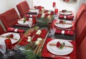 a colorful Christmas tablescape with red placemats, red blooms, red glasses, evergreens and pinecones and red napkins is bold and chic