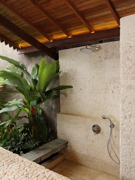 A neutral indoor outdoor bathroom with stone inspired tiles, a shower and statement tropical plants