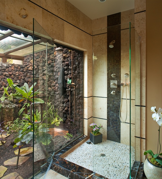 An indoor outdoor bathroom with neutral walls, a glass enclosed shower with an entrance to an outdoor shower and tropical plants growing outdoors