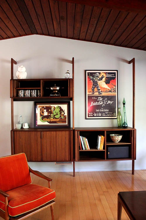 A mid century modern wooden wall unit with open and closed compartments and artworks