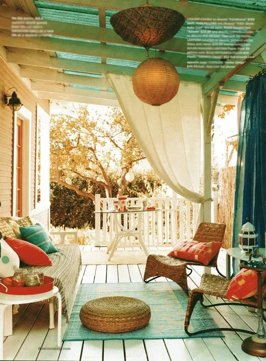 a boho porch with white wooden and woven furniture, orange and turquoise textiles, a jute ottoman and Moroccan lamps