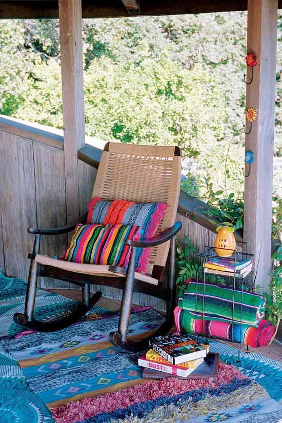 a colorful boho porch with bright printed textiles, a woven chair and colorful books stacked