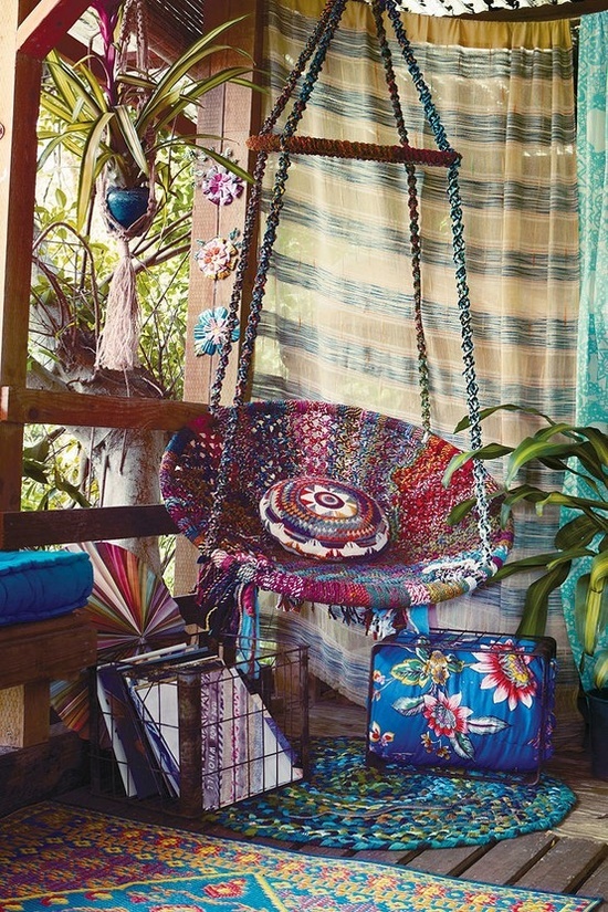 a bright gypsy porch with colorful curtains hanging, a woven hanging chair, colorful textiles and a bright rugs