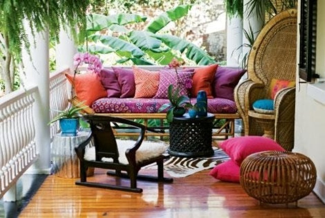 A colorful boho porch with woven and rattan furniture, colorful textiles, pinted rugs and bright pillows and greenery