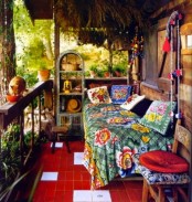 a super colorful boho porch with a relaxing nook – a daybed with colorful and printed floral textiles, a a woven storage unit, colorful furniture and greenery in pots