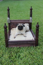 a refined dark-stained dog bed with pillars and tassels, with a neutral cushion is great for both indoors and outdoors