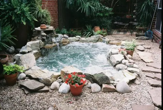 Beautiful in-ground natural-looking stone hot tub  surrounded by pebbles.