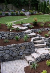 a stone garden path with stone walls around and several flower boxes with various greenery