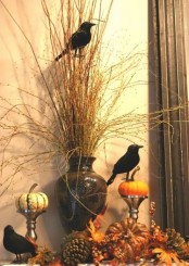 stylish Hallowene decor with a vase with branches, faux pumpkins, pinecones and leaves, blackbirds, stands with pumpkins