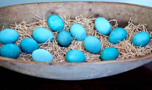 An Easter centerpiece of a whitewashed dough bowl, hay and blue Easter eggs