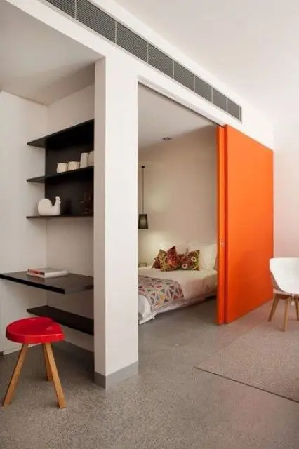 a bright orange sliding door adds color to the space and saves it