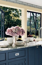 a modern farmhouse kitchen with navy cabinets, white marble countertops and large windows with lovely and relaxing garden views