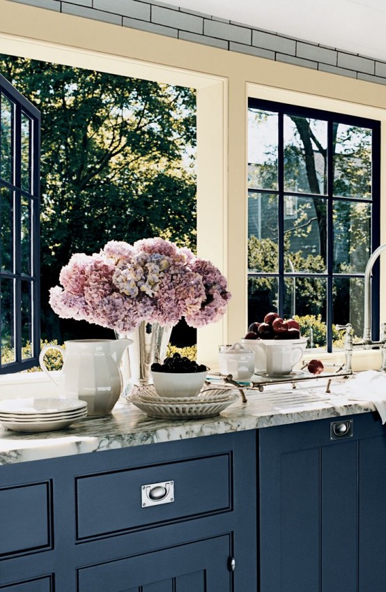 a modern farmhouse kitchen with navy cabinets, white marble countertops and large windows with lovely and relaxing garden views
