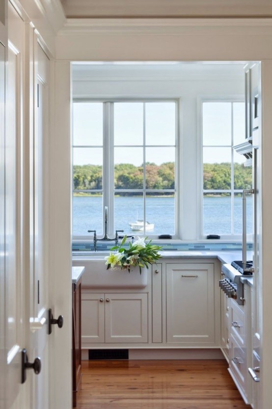 a vintage farmhouse kitchen with white shaker style cabinets, white stone countertops, large windows and a sea or lake view that creates an impression