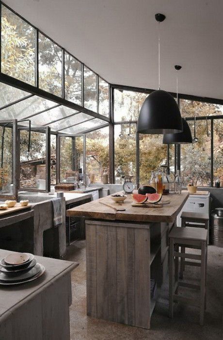 A jaw dropping wabi sabi kitchen with glazed walls and partly ceiling to merge with the forest outside, reclaimed and aged wood and concrete furniture and black pendant lamps