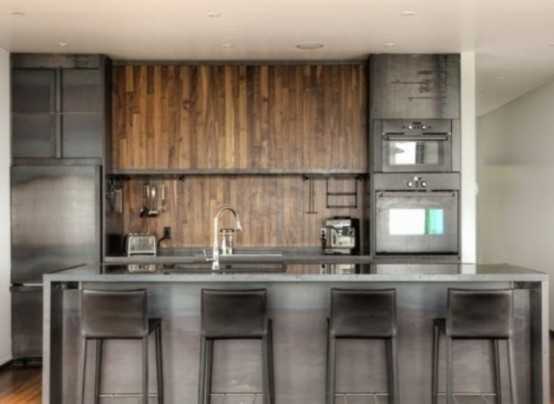 an industrial kitchen with metal cabinets and appliances, a wooden backsplash and cabinets, a metal kitchen island and stools for a masculine feel