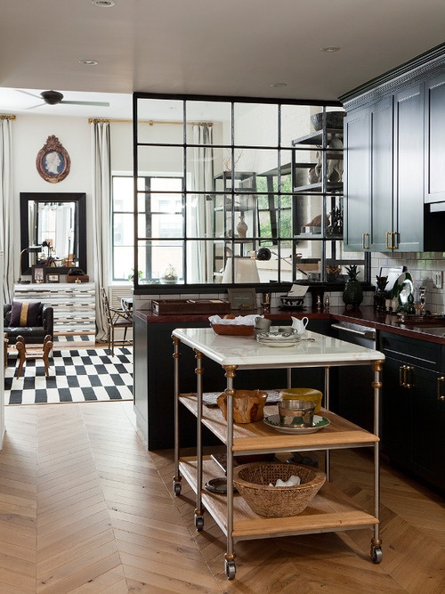 A moody kitchen with dark kitchen cabinets and light colored wooden countertops and a marble kitchen island