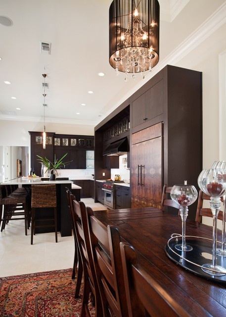 A rich stained wooden kitchen with white countertops, white backsplashes and lamps and woven stools