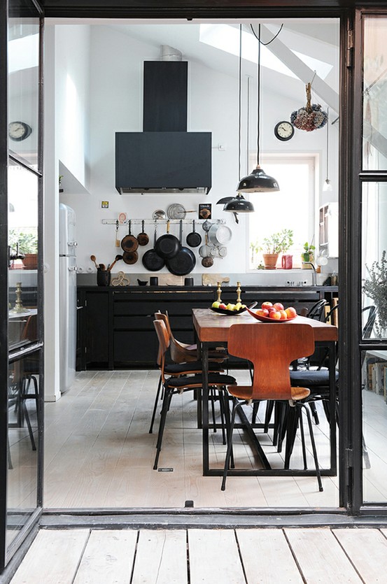 A black metal kitchen with pendant lamps, a black hood, rich stained wooden dining set is very eye catchy