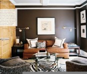 a dark living room with black walls, upholstered and leather furniture, metal lamps, artworks and a glass coffee table