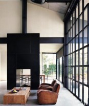 a contemporary living room with a glass wall, a black tile stove, leather chairs and a wooden coffee table