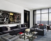 a contemporary masculine living room with dark upholstered furniture, some glass tables, an artwork and a glass wall for views