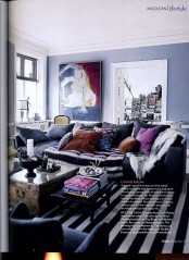 a moody living room with blue walls, dark furniture, printed pillows and an artwork plus a wooden chest coffee table