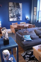a bright masculine living room with blue walls, comfy upholstered furniture, bright accents and an artwork