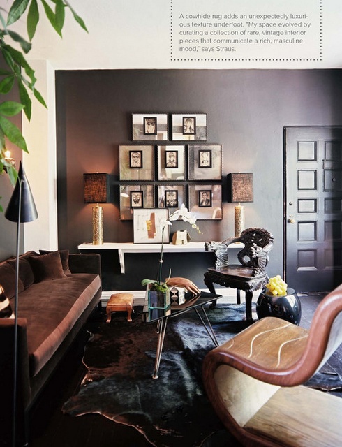 a dark masculine living room with dark walls, refined upholstered furniture, chic lamps, artworks and a catchy glass coffee table